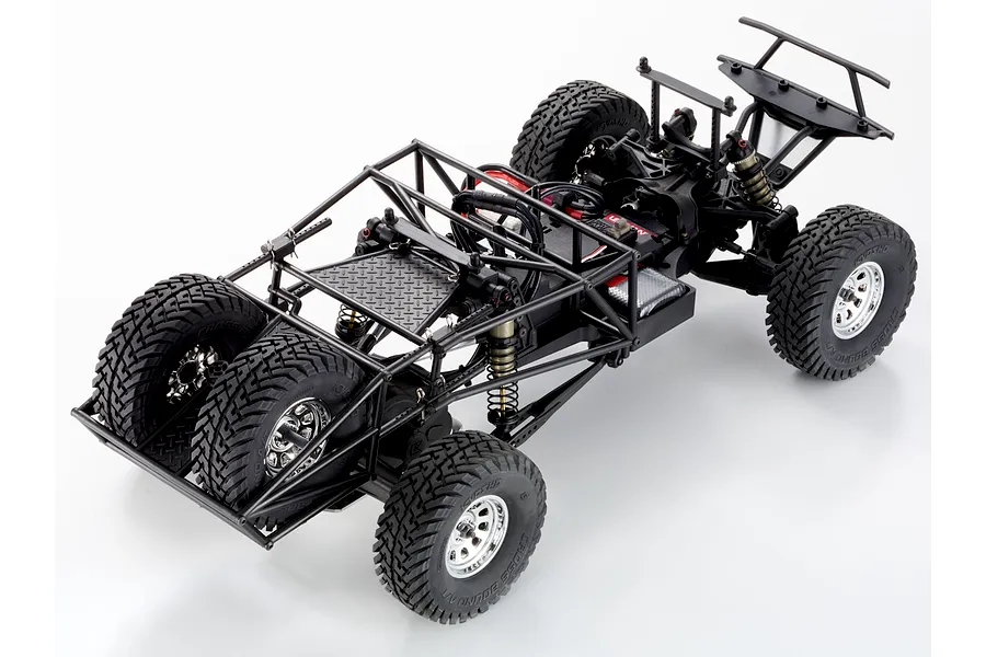 High angle studio view of the RC short course truck chassis without a body, showing its roll cage, spare tires, and suspension setup.