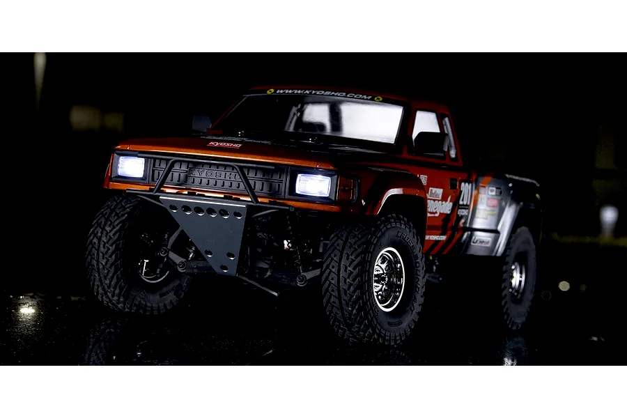Kyosho Outlaw Renegade 2WD short course RC truck in red and black with illuminated headlights parked outside at night.