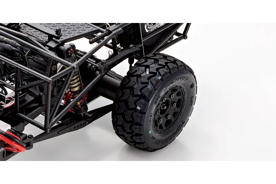 Close-up of the rear suspension and knobby tire on a Kyosho Outlaw Renegade 1/10 scale RC short course truck against a white background.