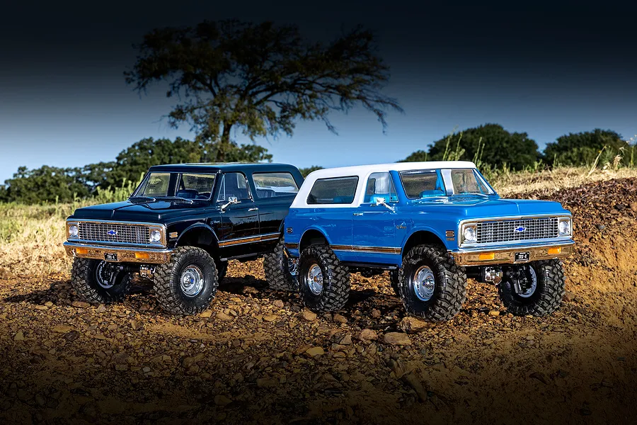 Two Traxxas TRX-4 Chevrolet Blazer RC rock crawlers in black and blue parked outdoors on rocky terrain.