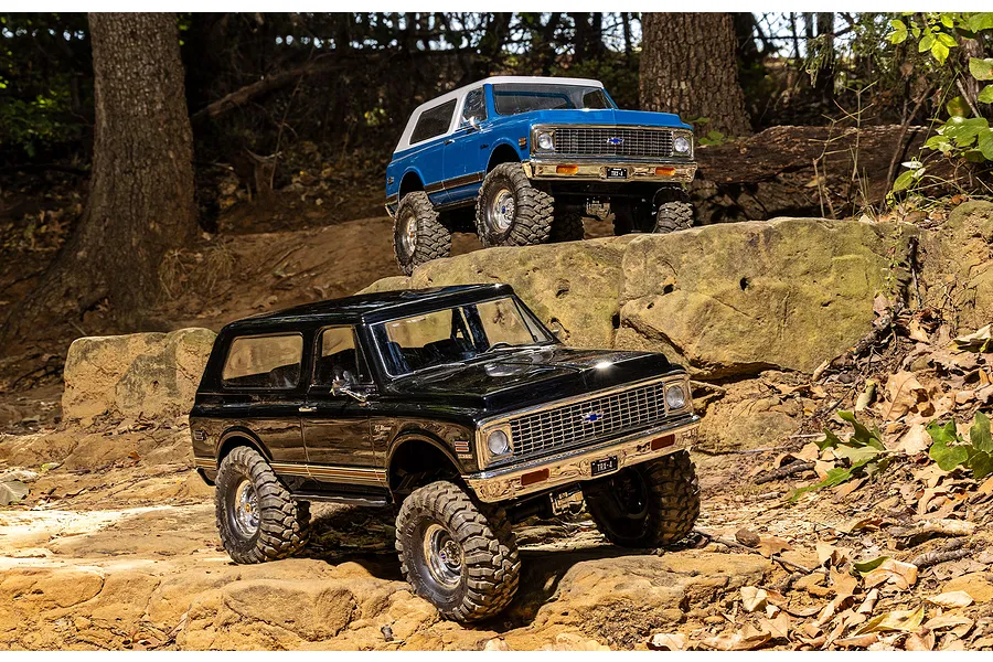 Two Traxxas TRX-4 Chevrolet Blazer RC rock crawlers in black and blue parked on rocky terrain outdoors.