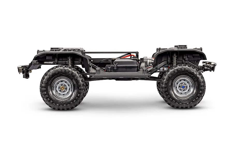 Side view of the bare Traxxas TRX-4 RC crawler chassis without body shell, showing frame rails, suspension, and wheels against a white background.