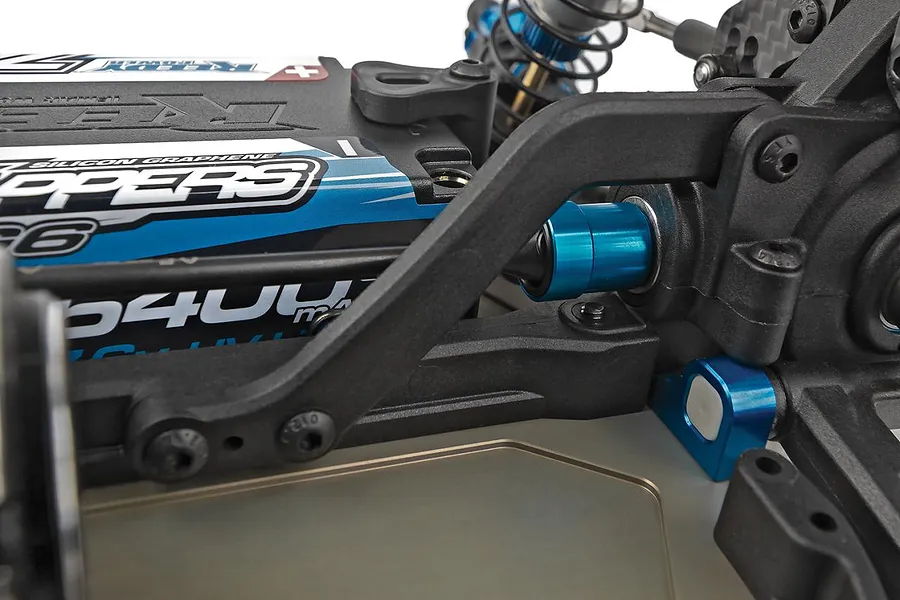 Close-up of RC buggy chassis showing black plastic suspension arm, blue anodized aluminium hardware, and a branded LiPo battery.