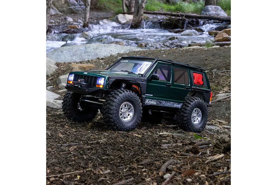 Axial SCX10 III Jeep Cherokee XJ RC rock crawler in green navigating an outdoor rocky stream bed.