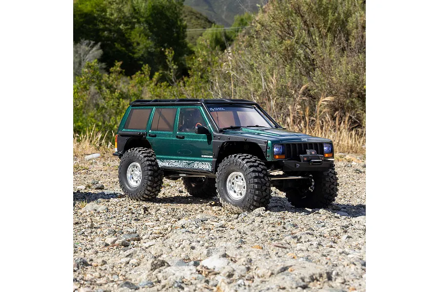 Axial SCX10 III Jeep Cherokee XJ RC rock crawler parked outdoors on rocky ground with green foliage in the background.