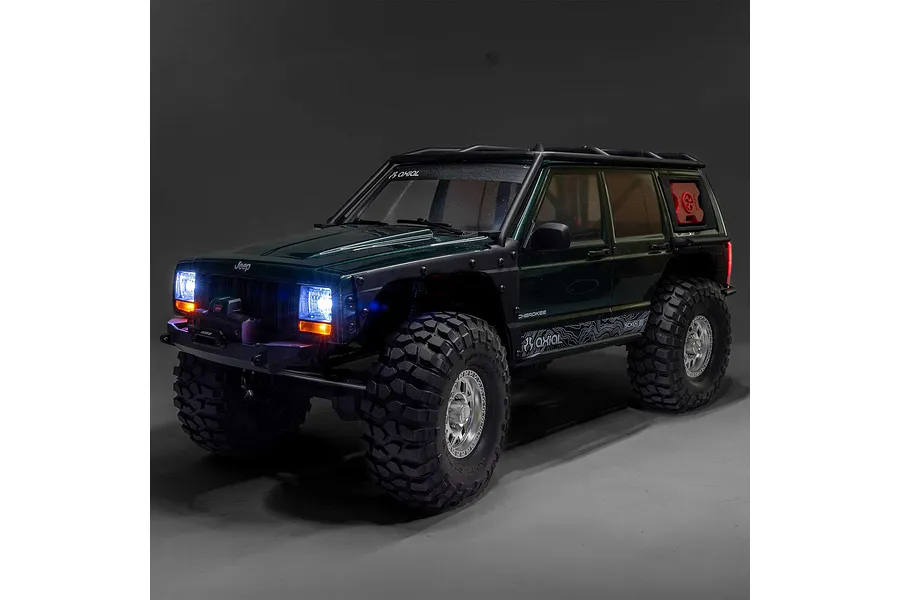 Axial SCX10 III Jeep Cherokee XJ RC rock crawler in dark green with lit headlights and off-road accessories.