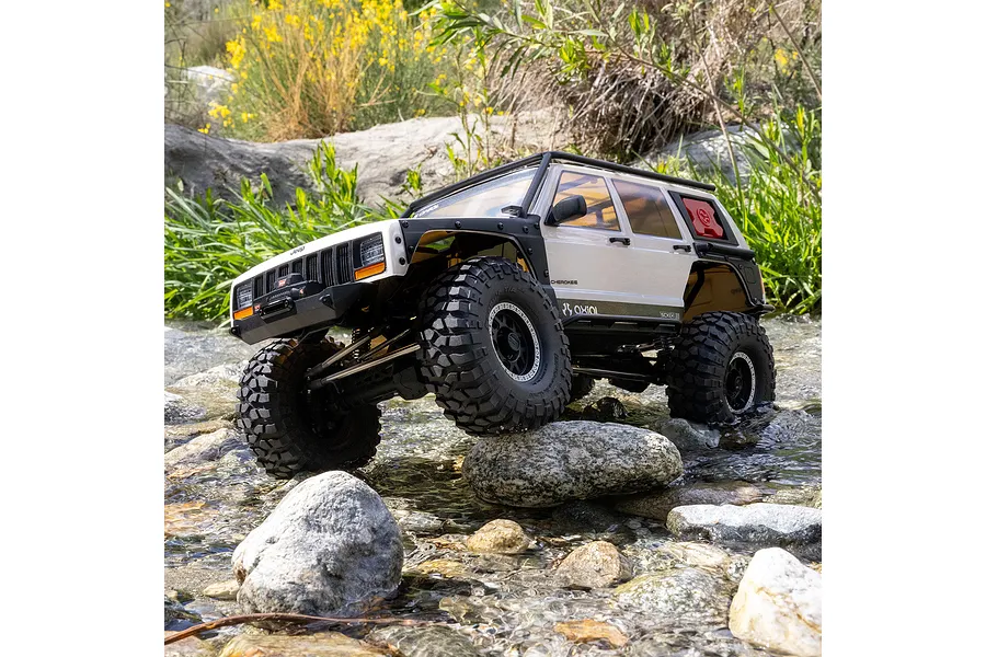 Axial SCX10 III Jeep Cherokee XJ RC rock crawler driving through a shallow rocky stream outdoors.