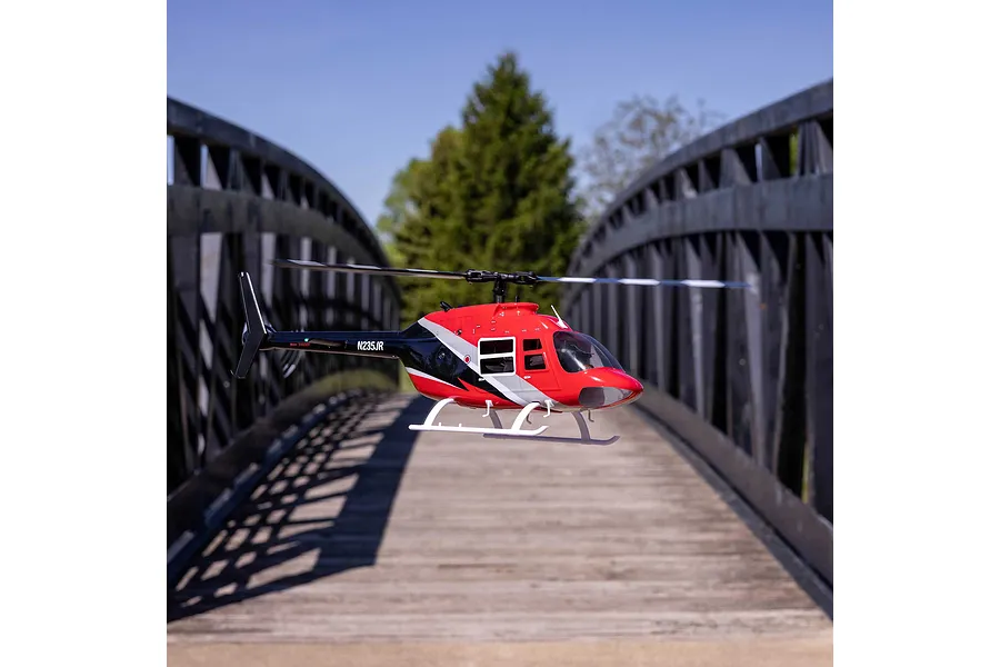 Blade Jet Ranger 235CP RC helicopter hovering outdoors on a wooden bridge with metal railings against a blue sky.
