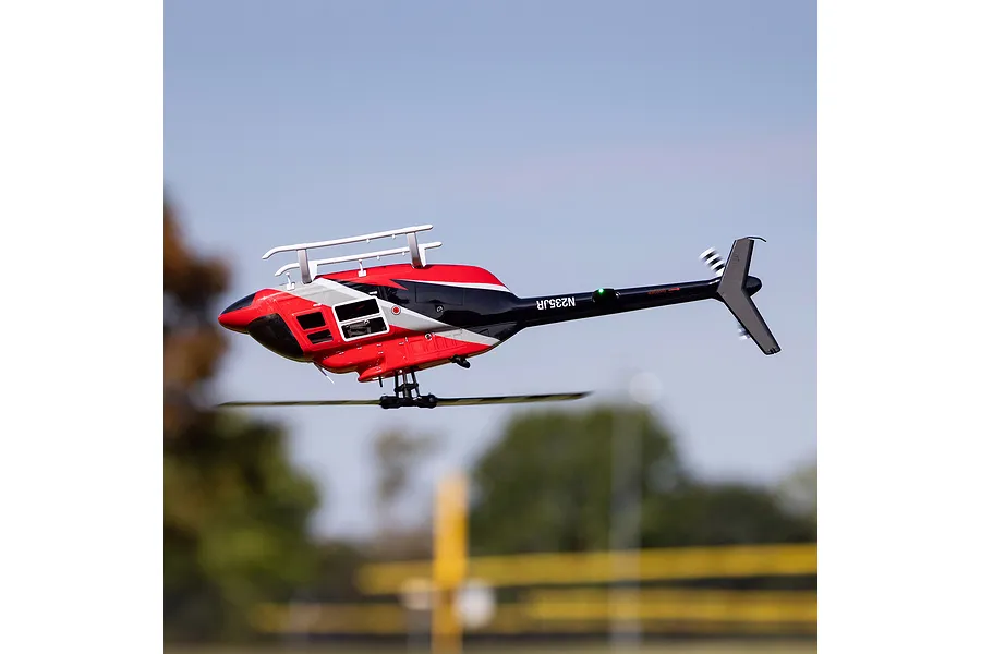 Blade Jet Ranger 235CP RC helicopter in flight outdoors against a clear blue sky and blurred green trees.