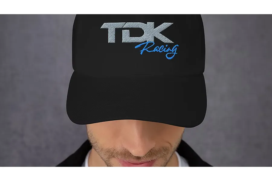 A person wearing a black dad hat featuring an embroidered TDK Racing logo on the front.