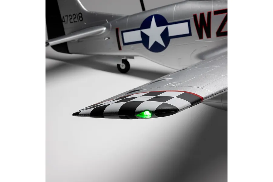 Close-up of the silver P-51D Mustang RC airplane wingtip showing a glowing green light and black-and-white checkered pattern.