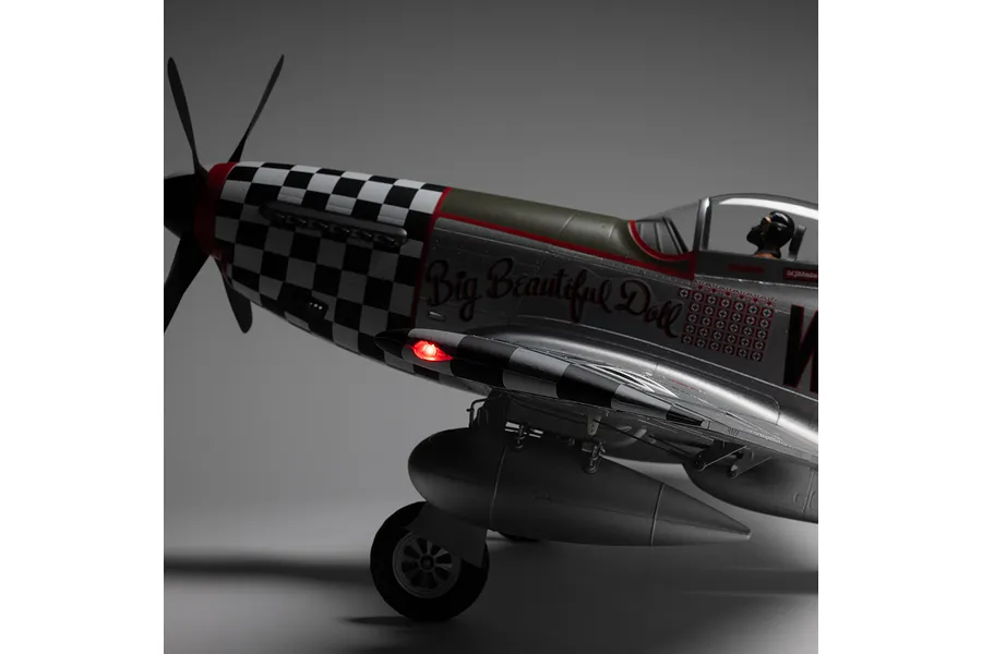 Close-up studio view of the nose section and wing of the E-Flite P-51D Mustang Big Beautiful Doll RC model, highlighting the glowing red wing light and checkered nose details.