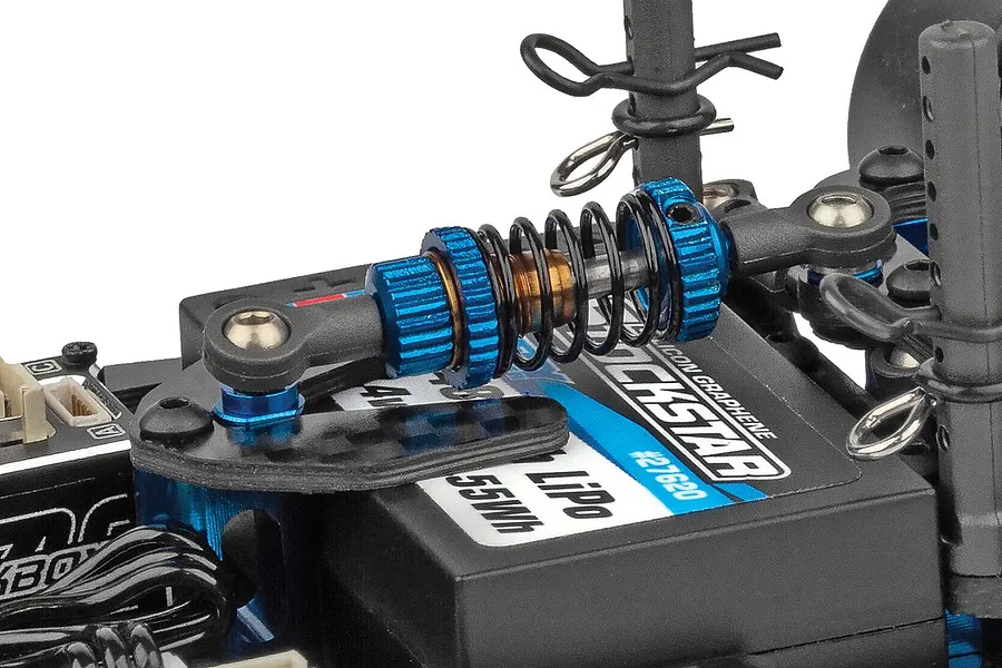 Close-up of a blue and black RC car shock absorber mounted horizontally over a battery in a chassis.
