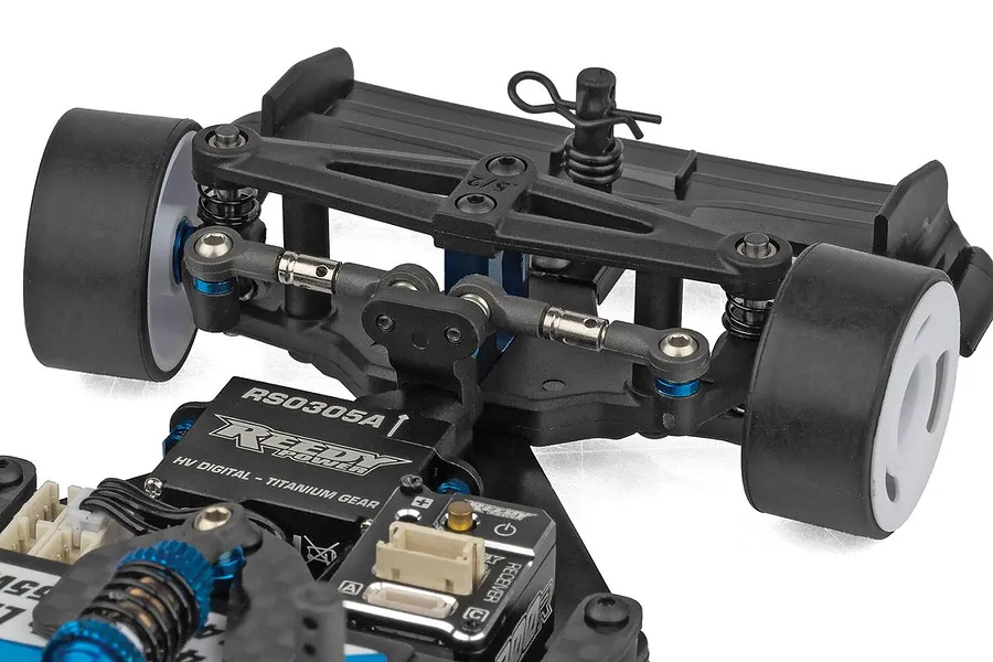 Close-up studio view of the rear suspension, carbon fibre shock tower, black wing, and Reedy servo on an RC car chassis.