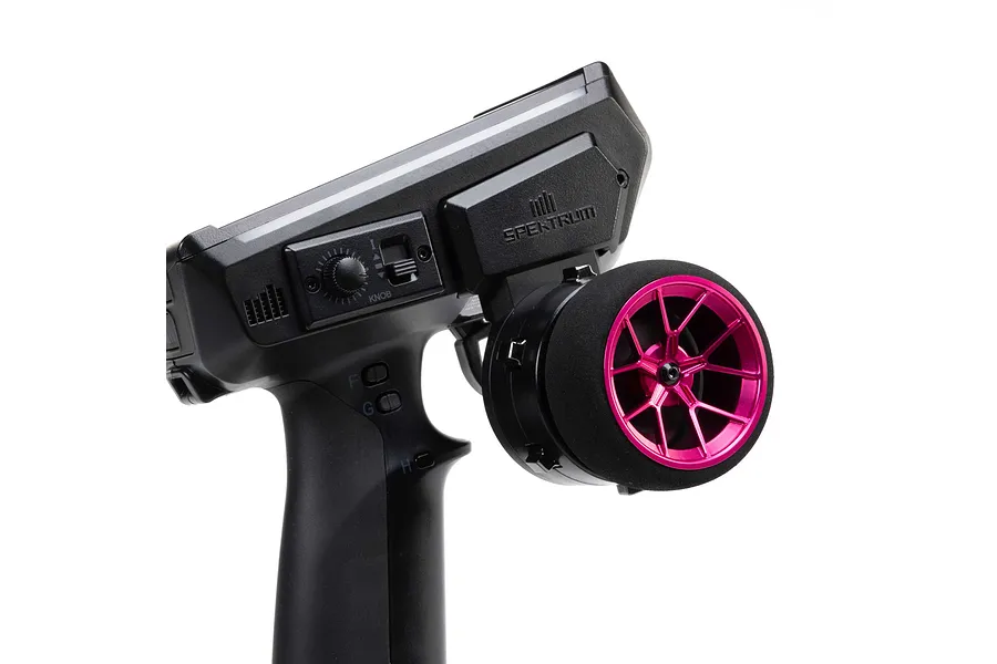 Close-up of a black RC transmitter with a bright pink wide spoke aluminium steering wheel and foam grip on a white background.