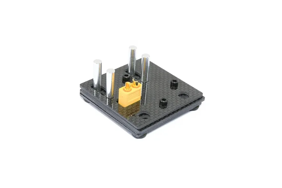Carbon fibre self-clamping soldering jig with four silver metal posts and a yellow XT connector held on a white background.