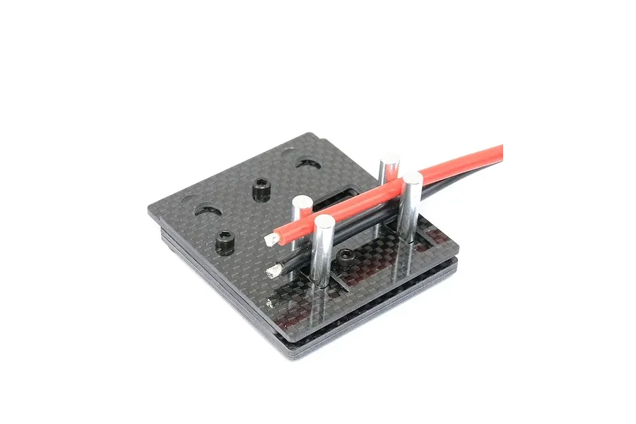 Carbon fibre self-clamping soldering jig holding red and black electrical wires between metal posts against a white background.
