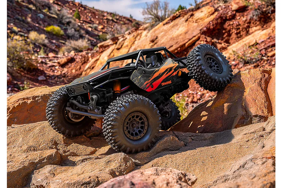 Traxxas RC rock crawler climbing rugged red rock terrain outdoors in a natural landscape setting.