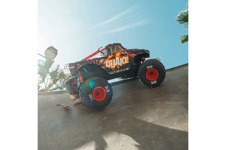 ARRMA Quake 4S RC monster truck driving outdoors on a concrete ramp under a bright blue sky.