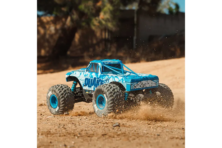 ARRMA Quake 4S blue monster truck kicking up dirt and sand in action on an outdoor dirt track.