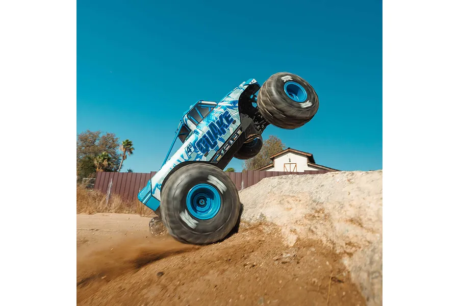 Blue ARRMA Quake 4S RC monster truck performing a wheelie on an outdoor dirt ramp.