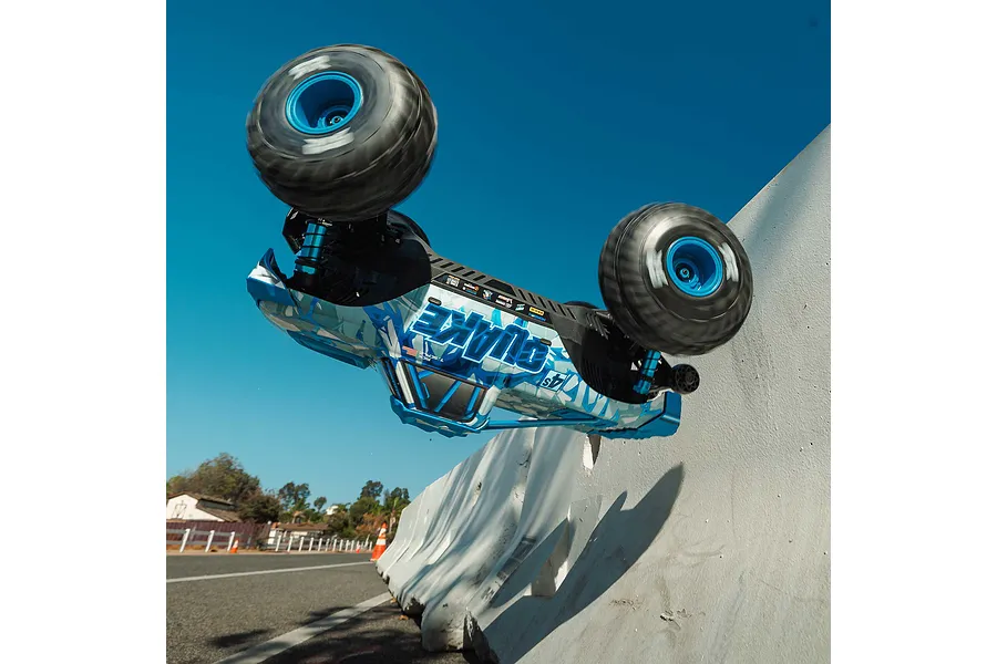ARRMA Quake 4S RC monster truck performing an action stunt, launching vertically off a concrete barrier outdoors.