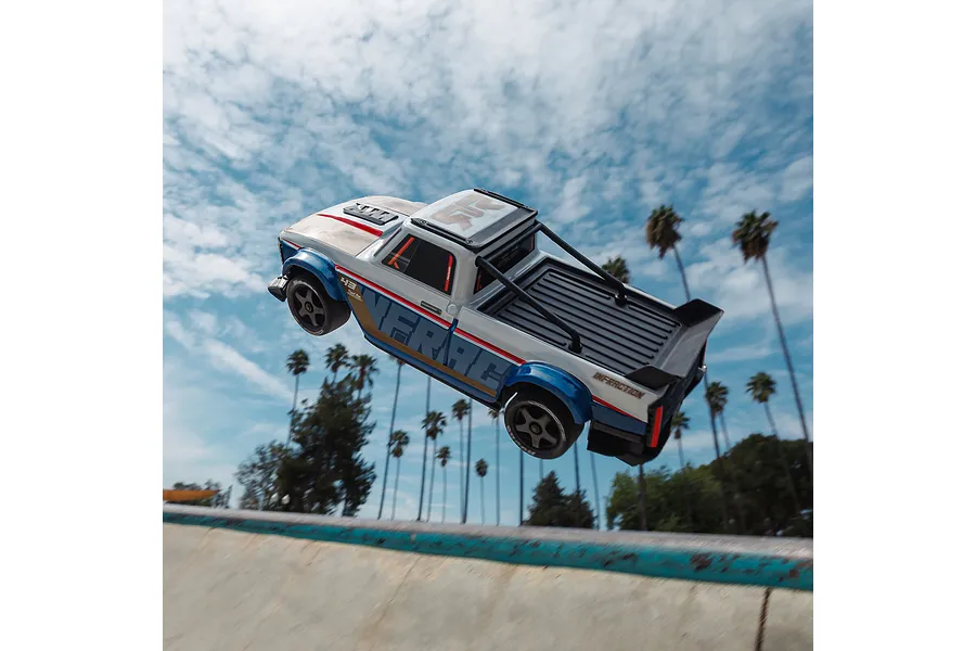 ARRMA Infraction RC truck airborne off a skate ramp against a blue sky with palm trees.