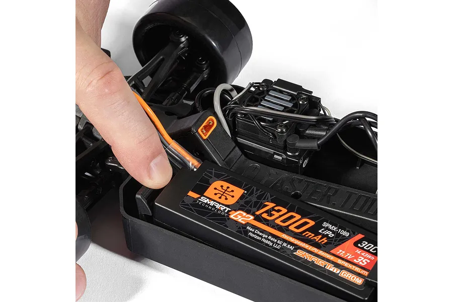 Close-up of a person installing a Spektrum Smart LiPo battery into an RC car chassis chassis.