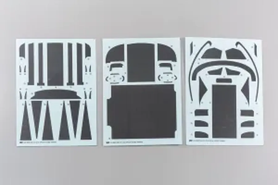 Three sheets of pre-cut black masking stickers laid out on a plain light grey studio background.