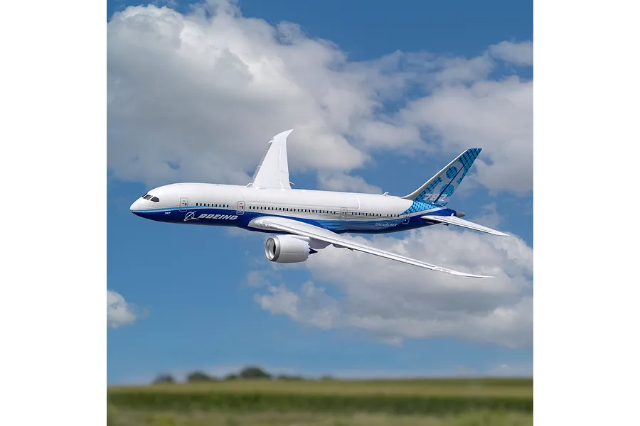 E-Flite Micro Boeing 787 Dreamliner RC plane flying in a blue sky with white clouds over a green field.