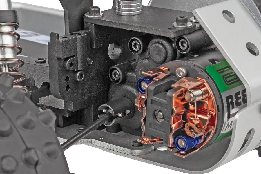 Close-up studio shot of the internal gearbox, motor brushes, and rear chassis assembly of a 1/10 scale RC buggy.