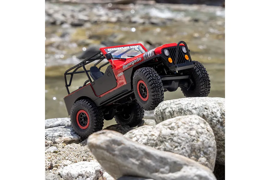 Axial SCX30 Jeep CJ-7 Renegade RC rock crawler in red navigating rocky terrain outdoors near water.