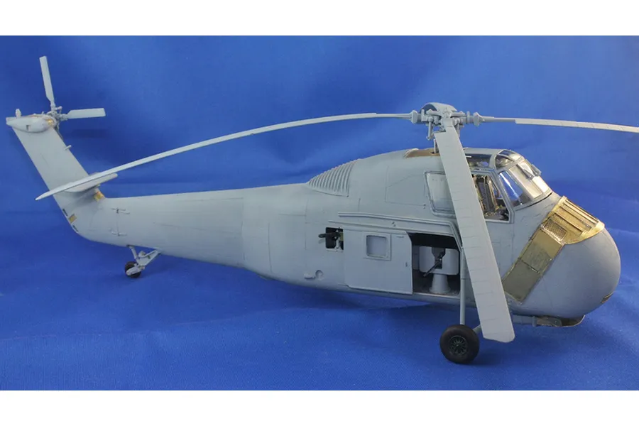 Assembled plastic model of an H-34 helicopter in light grey with brass photo-etch details against a blue background.