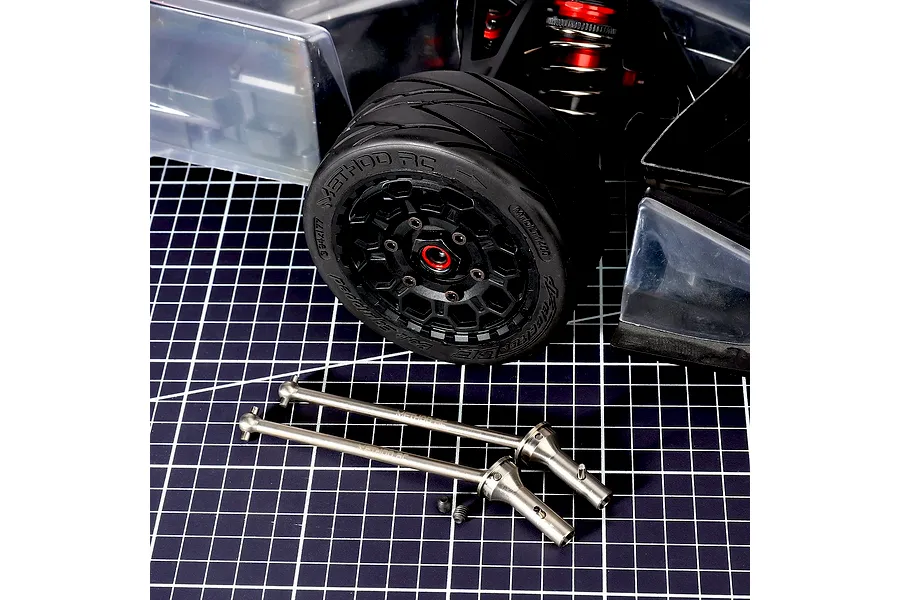Method RC titanium CVD driveshafts and small grub screws displayed on a cutting mat in front of an RC car wheel and chassis.