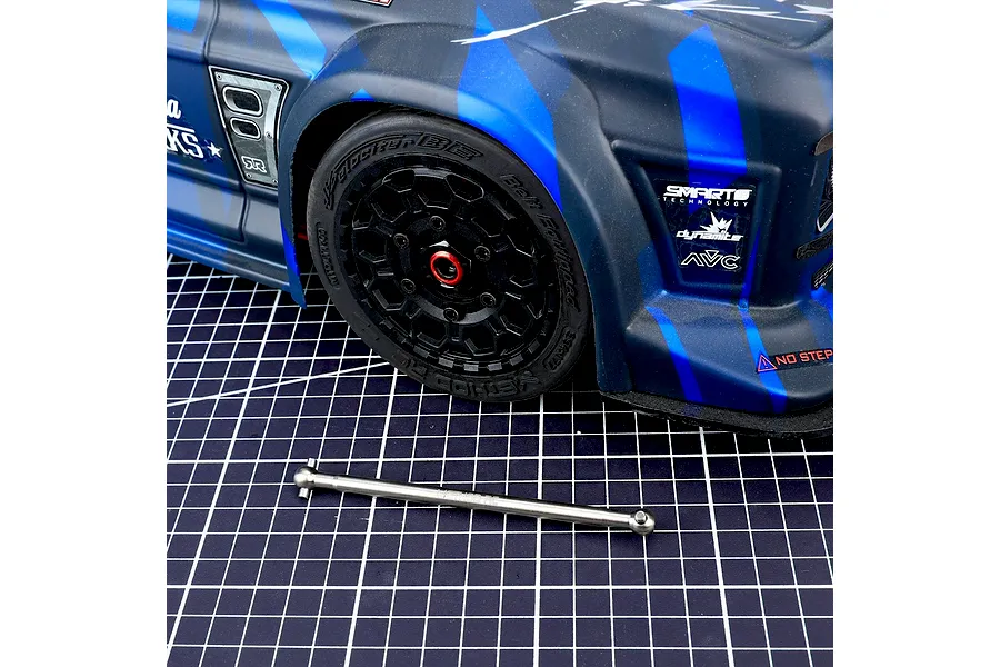 Method RC titanium driveshaft placed on a cutting mat in front of a blue and black RC car body and wheel.