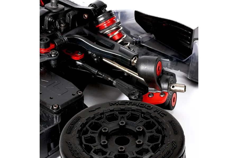 Close-up of an RC car suspension and drivetrain installed on a chassis, featuring a titanium driveshaft and a detached wheel in the foreground.