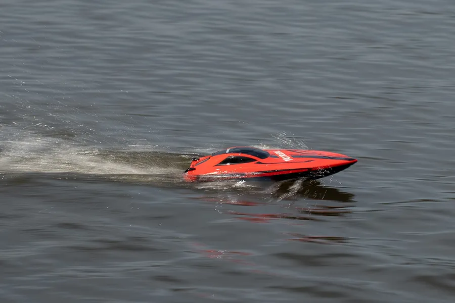 Red RC speed boat moving across water, creating a white wake spray during operation.
