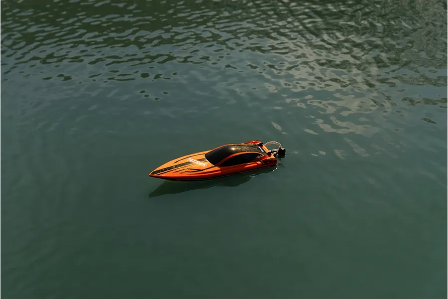 An orange Atrek Rogue RC speed boat floating on calm water in an outdoor setting.