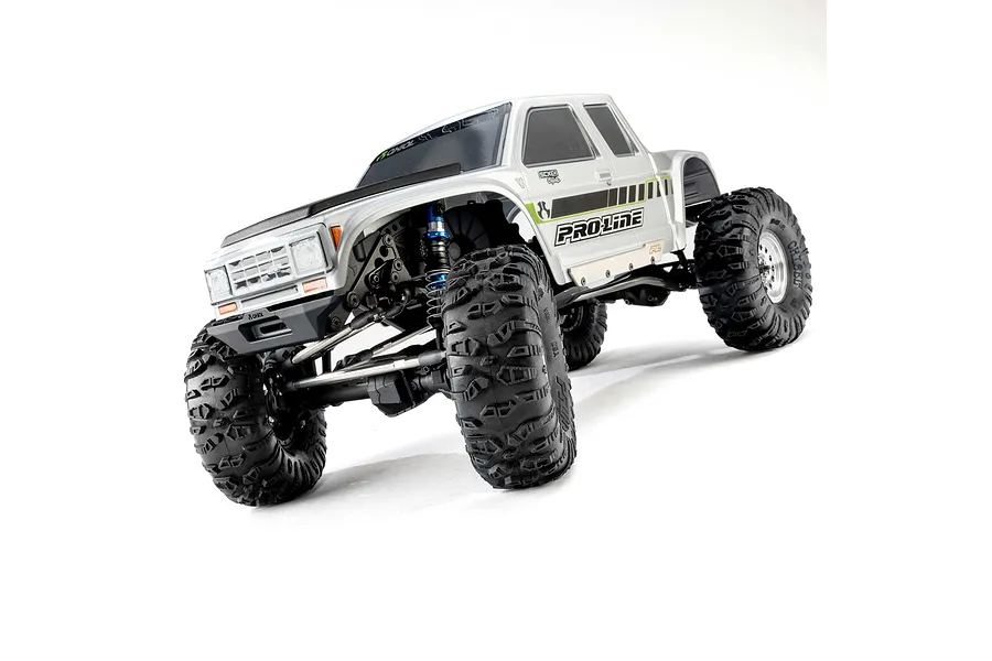 Low-angle shot of a silver RC crawler truck featuring Pro-Line Chisel II tyres mounted on wheels against a white studio background.