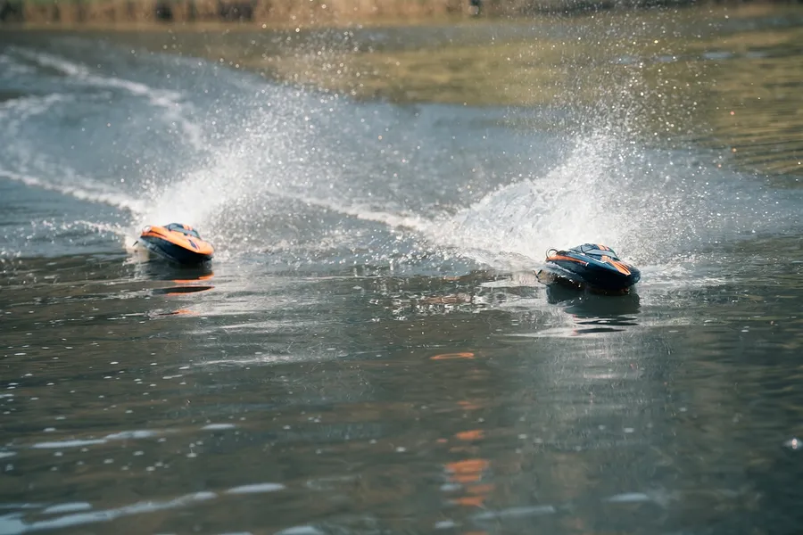 Two Atrek Stealth RC boats speeding across a lake, kicking up water spray and leaving wakes behind.