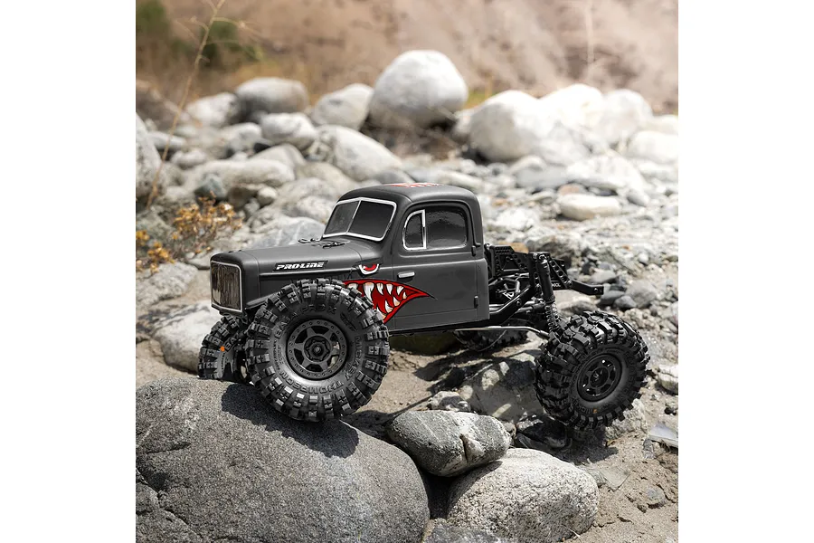 Pro-Line matte black cab-only crawler body mounted on an RC chassis traversing a rocky outdoor course.