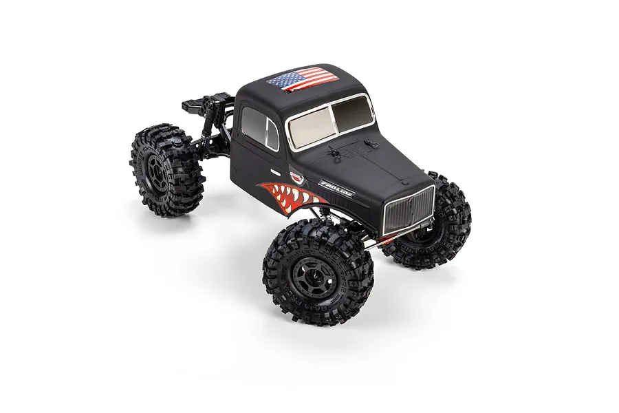 Matte black Pro-Line cab-only RC crawler body installed on a black chassis with oversized tires, shown against a white background.