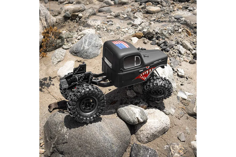 Pro-Line matte black cab-only crawler body mounted on an RC chassis traversing a rocky outdoor trail.