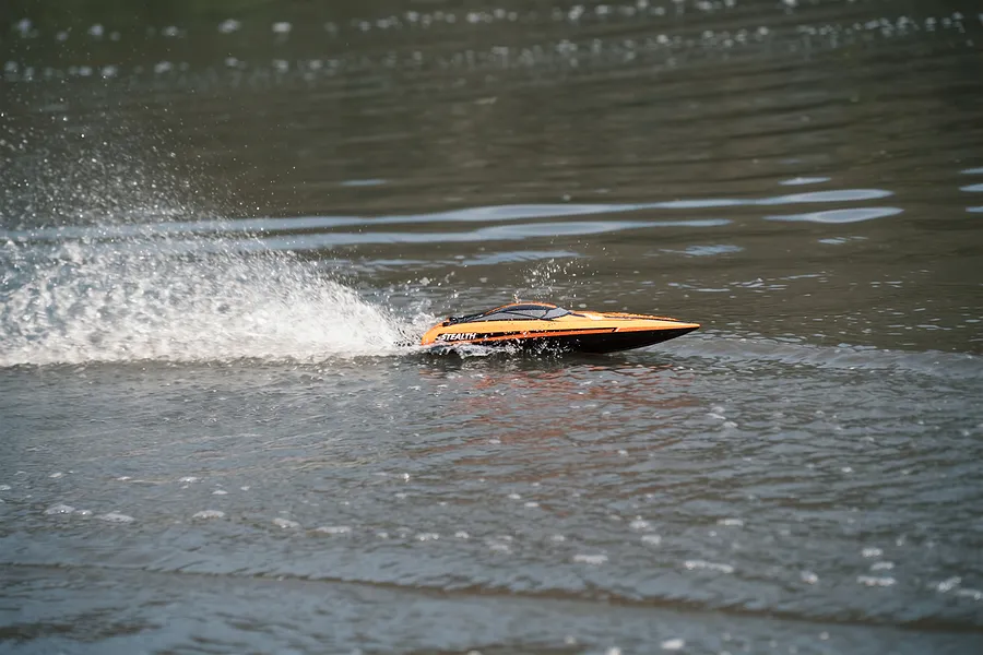 Atrek Stealth orange RC speed boat speeding across water, creating a white splash behind it.