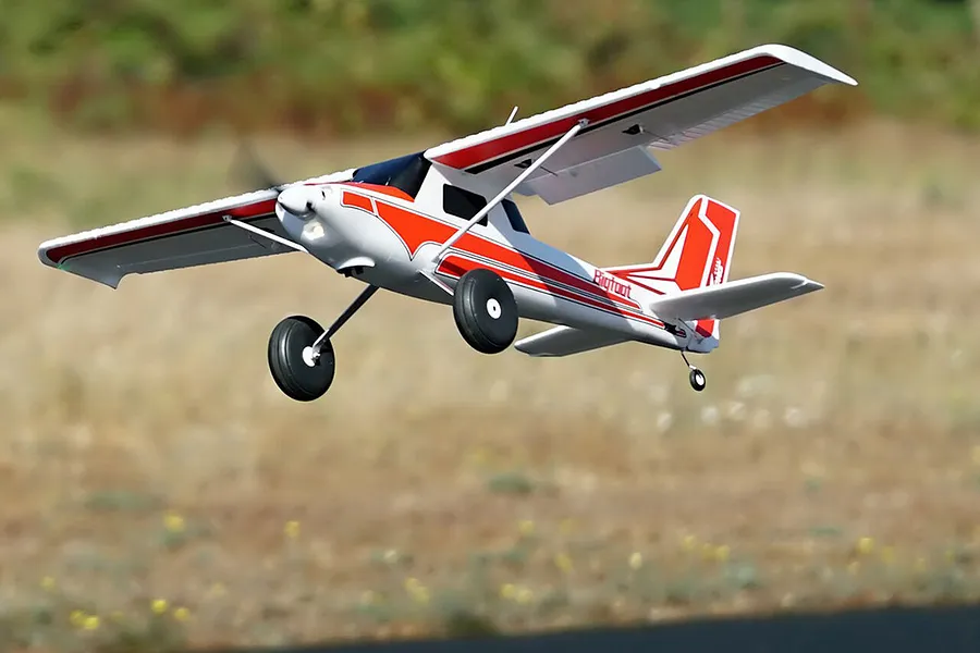 Arrows RC Bigfoot 1.3m trainer airplane in flight outdoors against a natural green and brown background