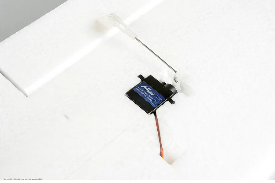 Close-up of an Arrows RC analog servo installed in white foam aircraft wing with pushrod linkage.