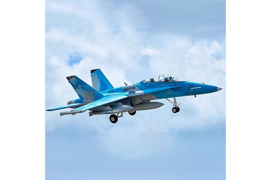 FMS RC F/A-18 Hornet jet in blue and grey livery flying against a cloudy sky background