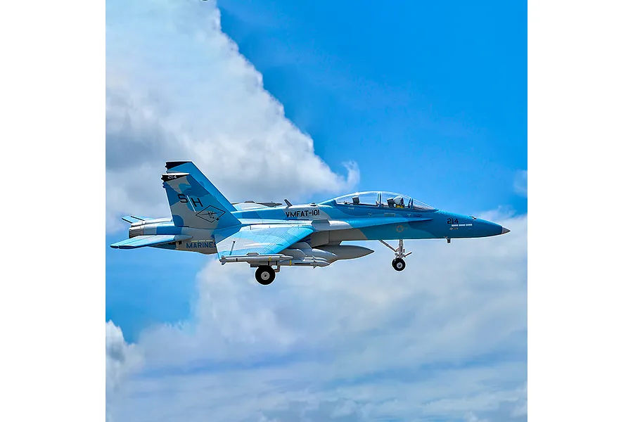 FMS F/A-18 Hornet RC jet airplane flying outdoors in a blue sky with white clouds, showing landing gear down.