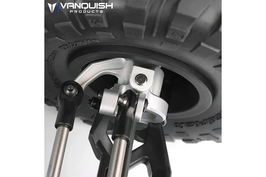Close-up of a silver aluminium steering hub installed on an RC vehicle, showing linkages and a tyre in the background.