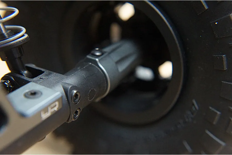 Close-up of a grey aluminium RC suspension arm with Yeah Racing logo installed on an Axial Wraith chassis.